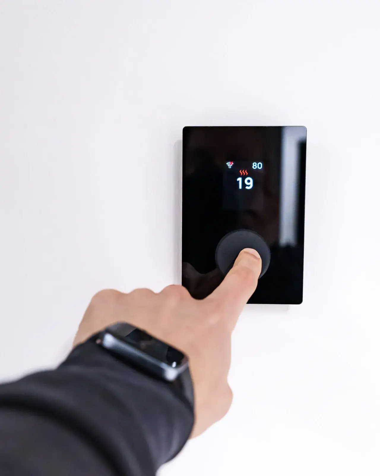 Close-up of a hand adjusting a wall thermostat set to heat